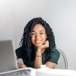 Happy ethnic woman sitting at table with laptop
