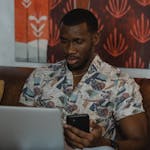 Man in White and Blue Floral Button Up Shirt Holding Black Smartphone